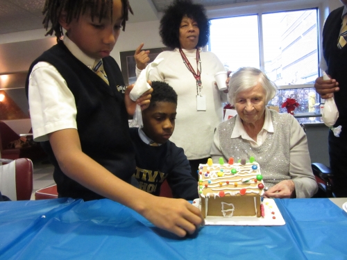 Homeland resident Janet Kepler and students from Nativity School recently collaborated on decorating gingerbread houses. Homeland Center resident and Nativity School students decorating gingerbread houses